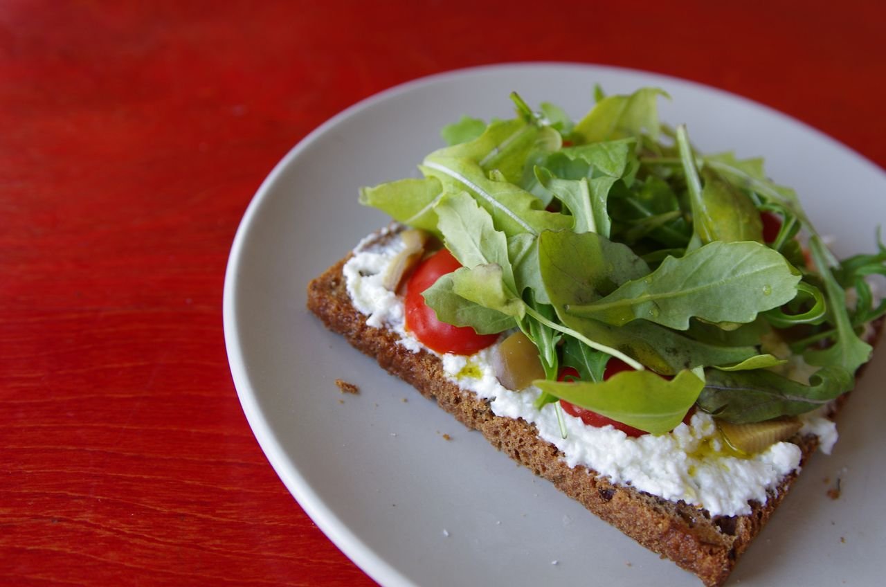Tasty open-faced sandwich with arugula, cheese, and tomatoes on a plate.